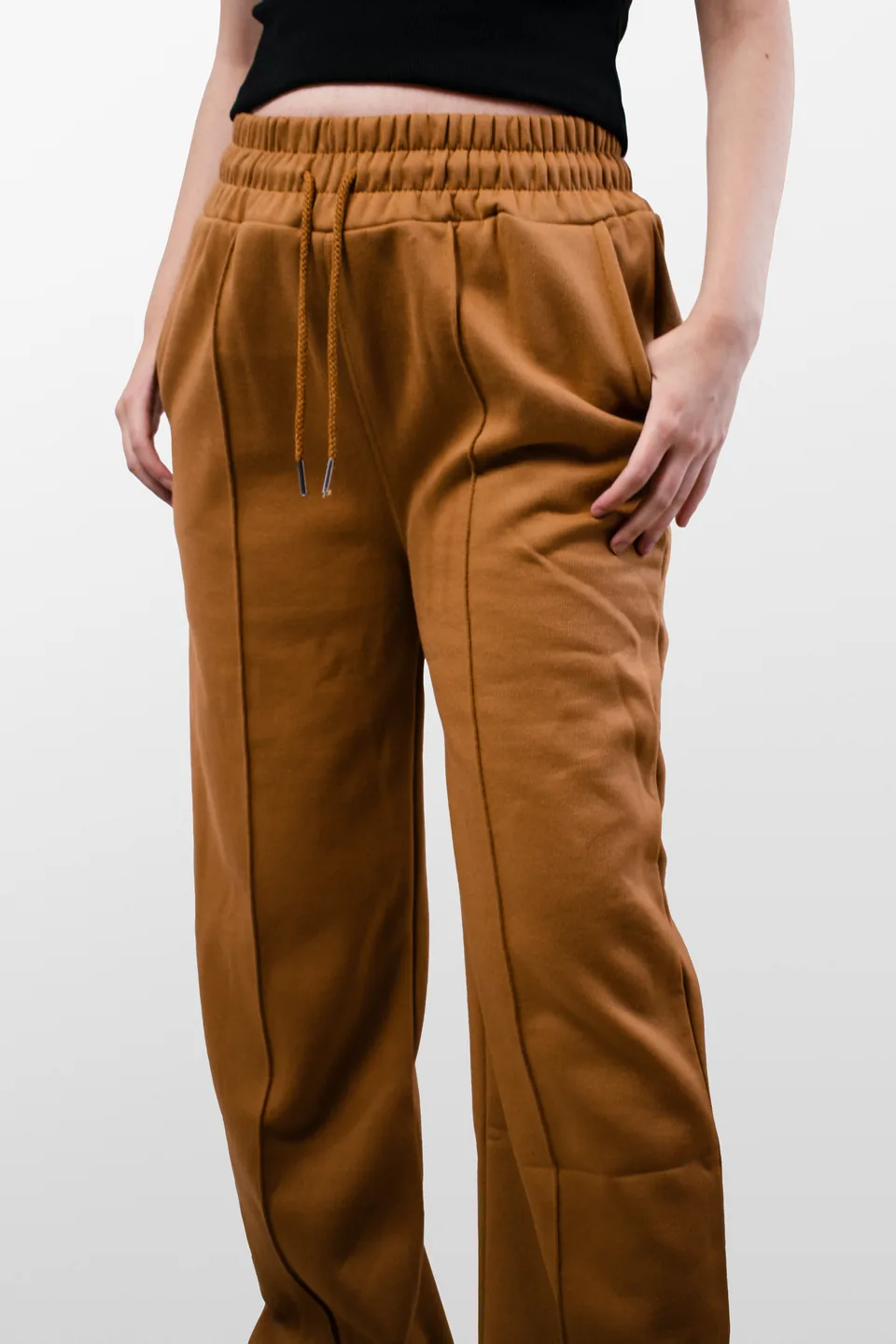 Detalle de la cintura elástica, cordones y bolsillo de un pantalón mostaza.
